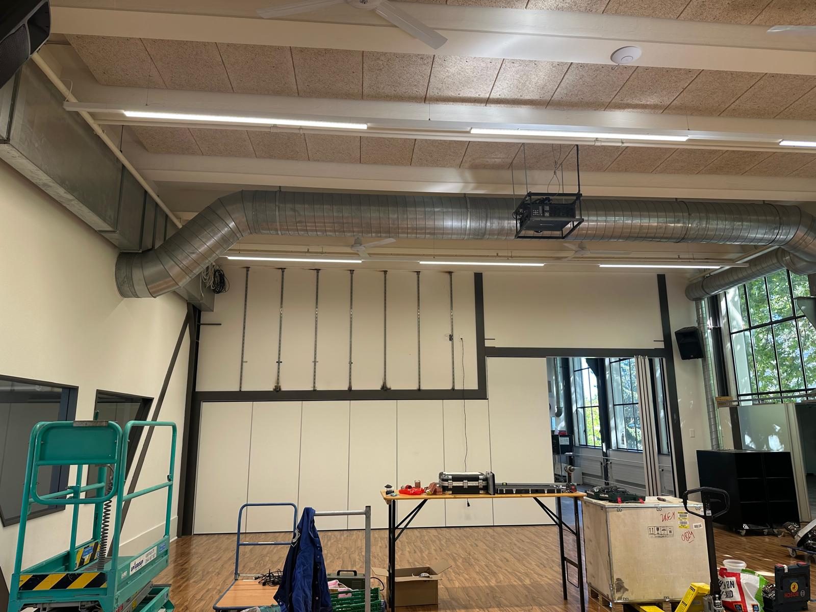 Workshopraum mit sieben senkrechten Montageschienen an der Stirnwand, darüber der bisherige Beamer an der Decke